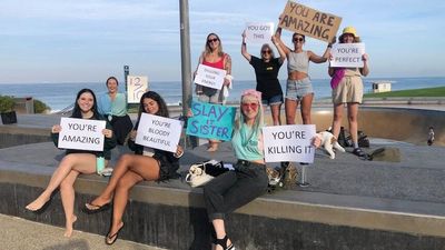 Women at Scarborough beach hold up encouraging signs for joggers in response to men rating women
