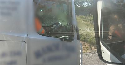 Lorry driver cruises truck down motorway with hands off wheel to roll cigarette