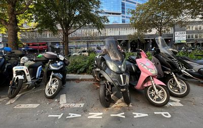 Resigned riders of gasoline-fueled motorbikes pay for parking in Paris