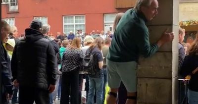 Edinburgh man watches Queen's procession while standing on stilts and gripping pillar