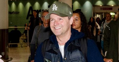 Declan Donnelly beams as he pushes baby son through Heathrow after landing in UK