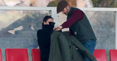 David Beckham wraps 'freezing' Victoria in his coat as they watch Romeo play football