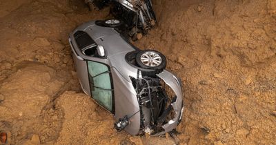 Enormous sinkhole delving deep into earth swallows two cars amid raging storm