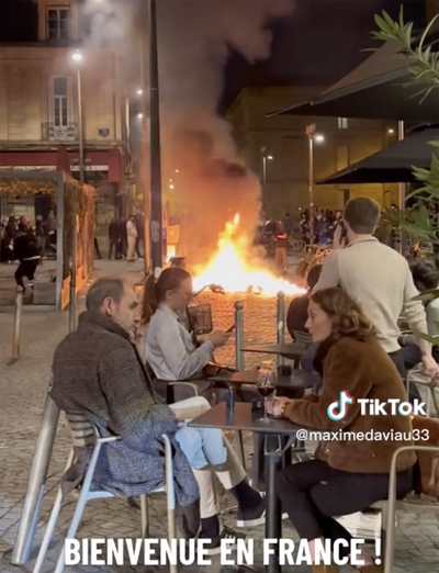 French diners enjoy glass of wine as city burns in background during Macron protests