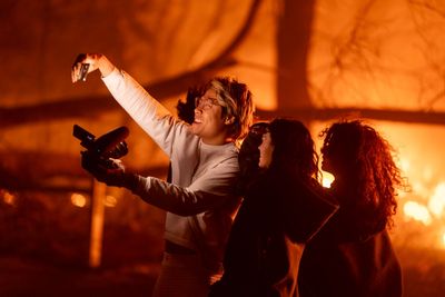 Gleeful young adults grin for selfies while deadly California wildfires roar behind them