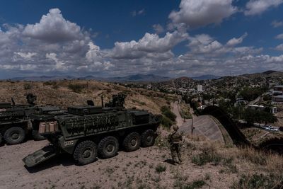 A man is halted climbing the US-Mexico border wall. Under new Trump rules, US troops sound the alarm