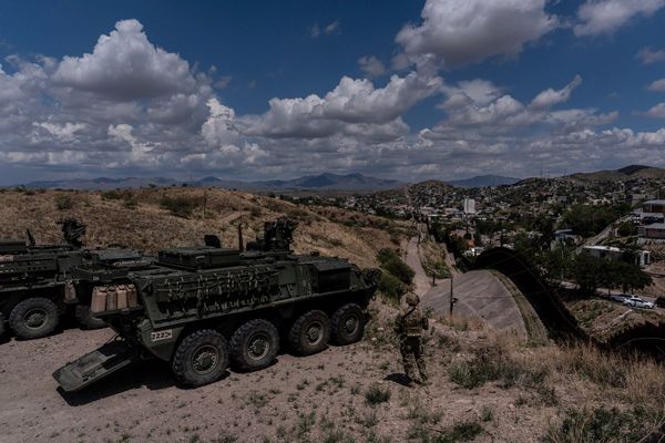 A man is halted climbing the US-Mexico border wall. Under new Trump rules, US troops sound the alarm
