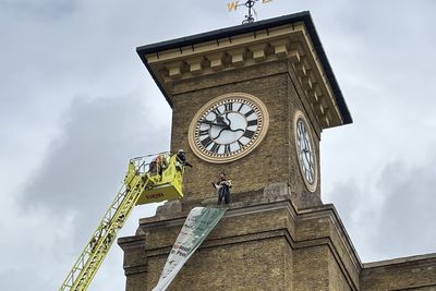 Protester clutching a dog climbs clocktower at mainline train station