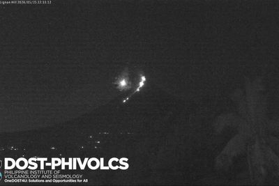 Moment meteor flies through sky beside erupting volcano
