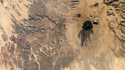 Shadowy tendrils of ancient lava have scarred a dark volcano next to a 'skull' in the Sahara — Earth from space